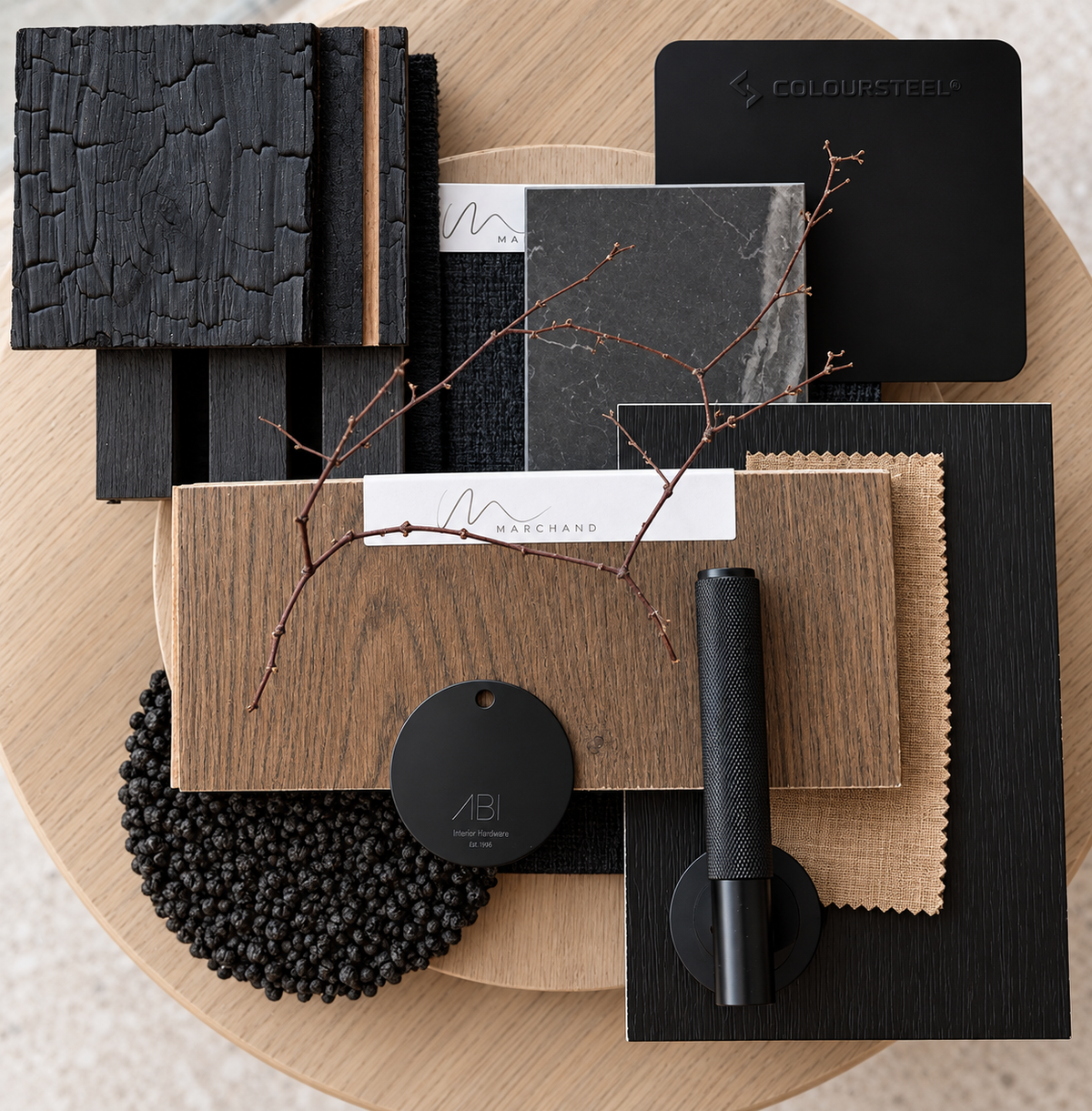 Dark and Moody concept box flatlay: a smoked oak sample board with charred timber, black marble, black leather and hardware, and a dried branch on a pale timber round